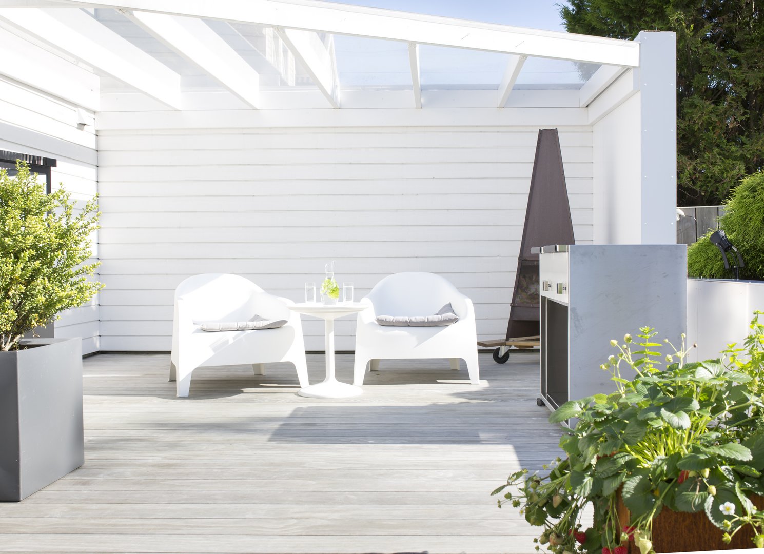 Bild einer hellen Ecke am Haus mit einer hellen Holzterrasse und 2 weißen Stühlen - überdacht