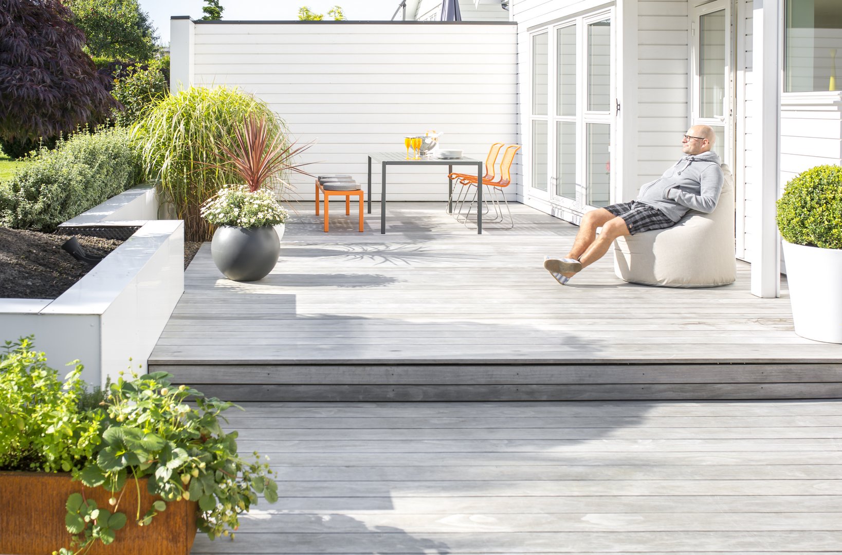 Ein Mann genießt die Sonne auf seiner  hellen Holzterrasse sitzend